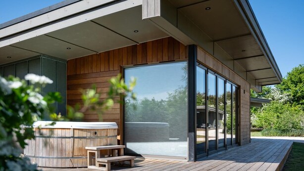 Una terraza moderna al aire libre con un jacuzzi, bancos de madera y un área de patio con paredes de vidrio.
