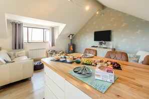 Un salon chaleureux avec une table à manger en bois, dressée pour le repas, une cheminée et un coin salon confortable.