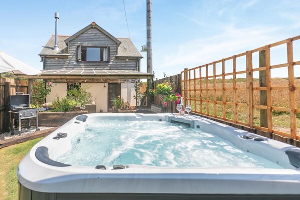 Un bain à remous dans un jardin, avec une clôture en bois, une maison et un barbecue.