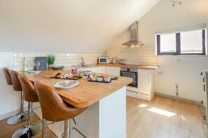 A modern kitchen with a central island, bar stools, a microwave, and a stove. - 2 Bed in Newquay (oc-82512) (Saint Newlyn East)