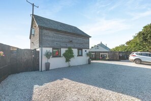 A two-story building with a sloped roof, a gravel driveway, and a fenced area with a parked car. - 2 Bed in Newquay (oc-82512) (Saint Newlyn East)