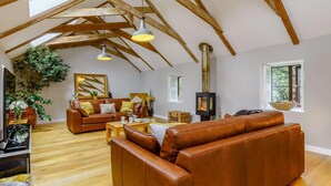 Un salon de style industriel, avec un plafond haut, des poutres en bois, une cheminée, des canapés en cuir et une grande fenêtre.