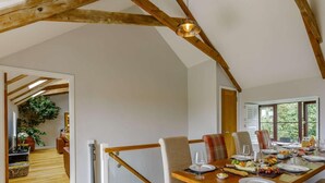 Un coin repas avec une table en bois dressée pour le repas, un escalier et une vue sur la verdure à l’extérieur.