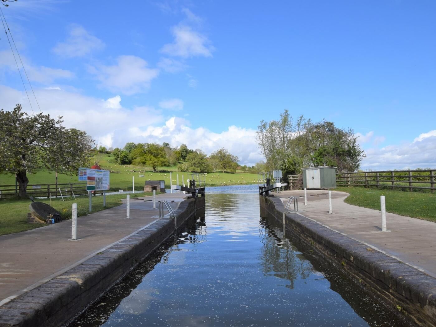 A canal with a lock system, a wooden fence, and a grassy area with trees.