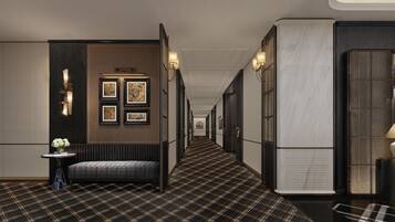 A corridor with a checkered floor, framed artwork on the walls, and a bench with a vase of flowers.