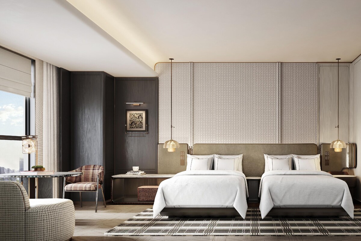 A hotel room with two beds, a desk, a chair, a view of the city, and a large window.