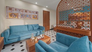 Una sala de estar con un sofá azul, una mesa de centro con un florero y una botella, y un separador de madera decorativo con un diseño geométrico.
