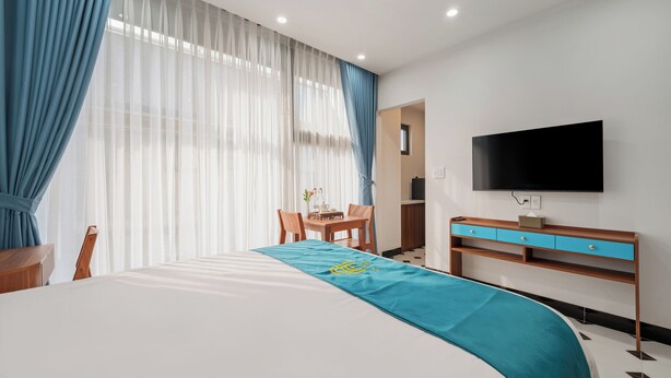 A hotel room with a bed, a desk, a chair, a television, and a window with curtains. - An Cuu Residence (Hue)