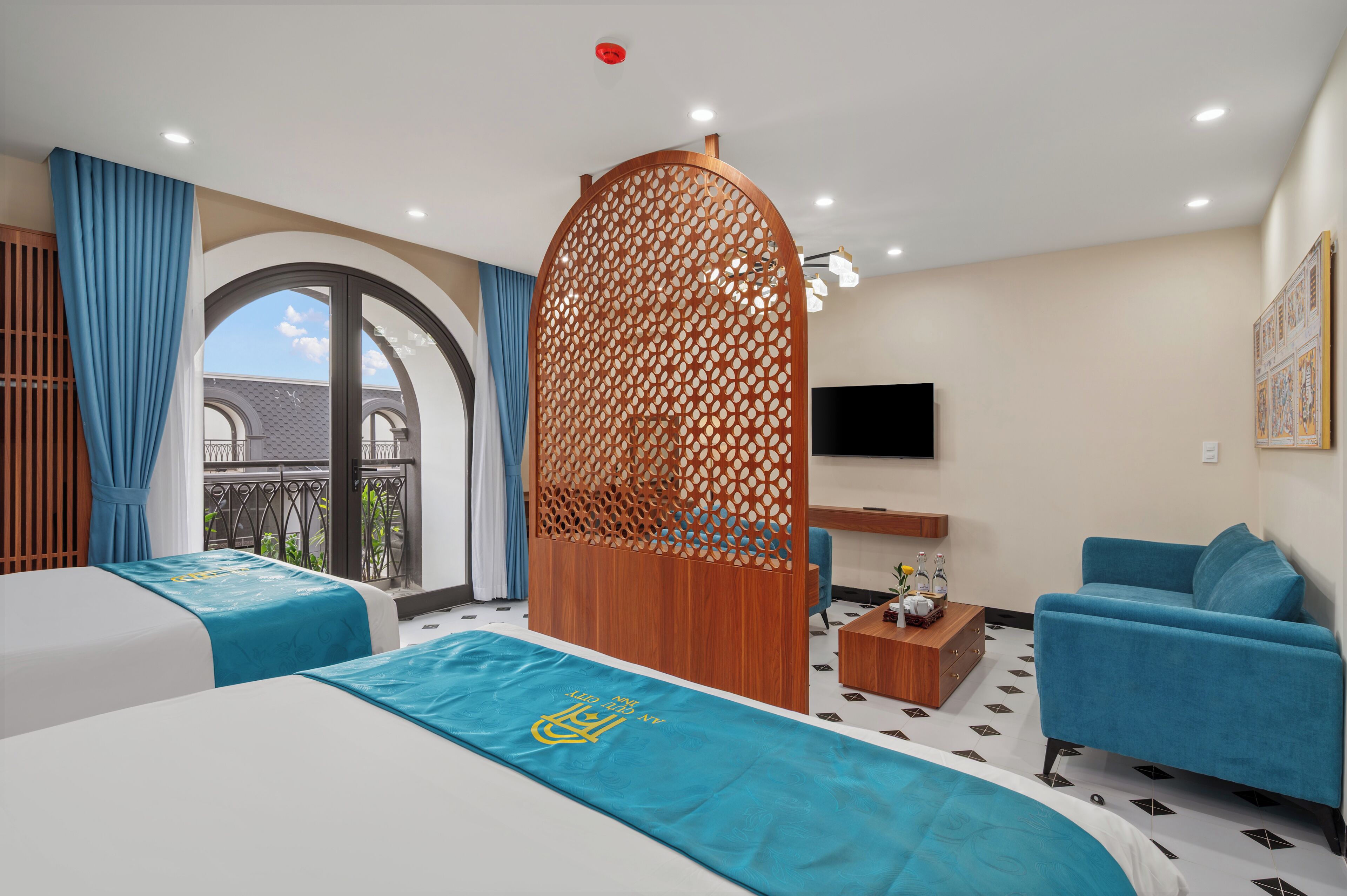 Habitación de hotel con dos camas, un sofá, un televisor y un balcón con cortinas azules.