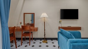 A hotel room with a desk, chair, mirror, lamp, TV, and a blue sofa. - An Cuu Residence (Hue)