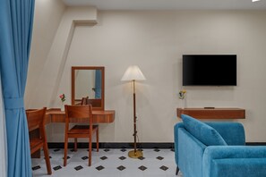 Habitación de hotel con escritorio, silla, espejo, lámpara, televisor y un sofá azul.