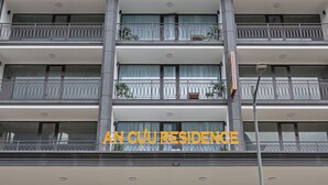 Un hotel de varios pisos con balcones, una entrada despejada y señalización que indica 'AN CUJ RESIDENCE'.