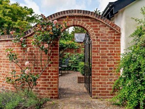 A brick archway leading to a garden with a bench and a gate. - 1 Bed in Lymington (oc-83370) (Sway)