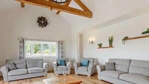 Een ruime woonkamer met een houten plafond, een groot raam met gordijnen en een houten salontafel.