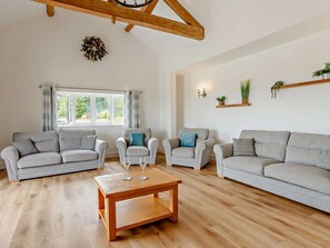 Ein geräumiges Wohnzimmer mit Holzboden, einem großen Fenster mit Vorhängen und einem Holztisch.
