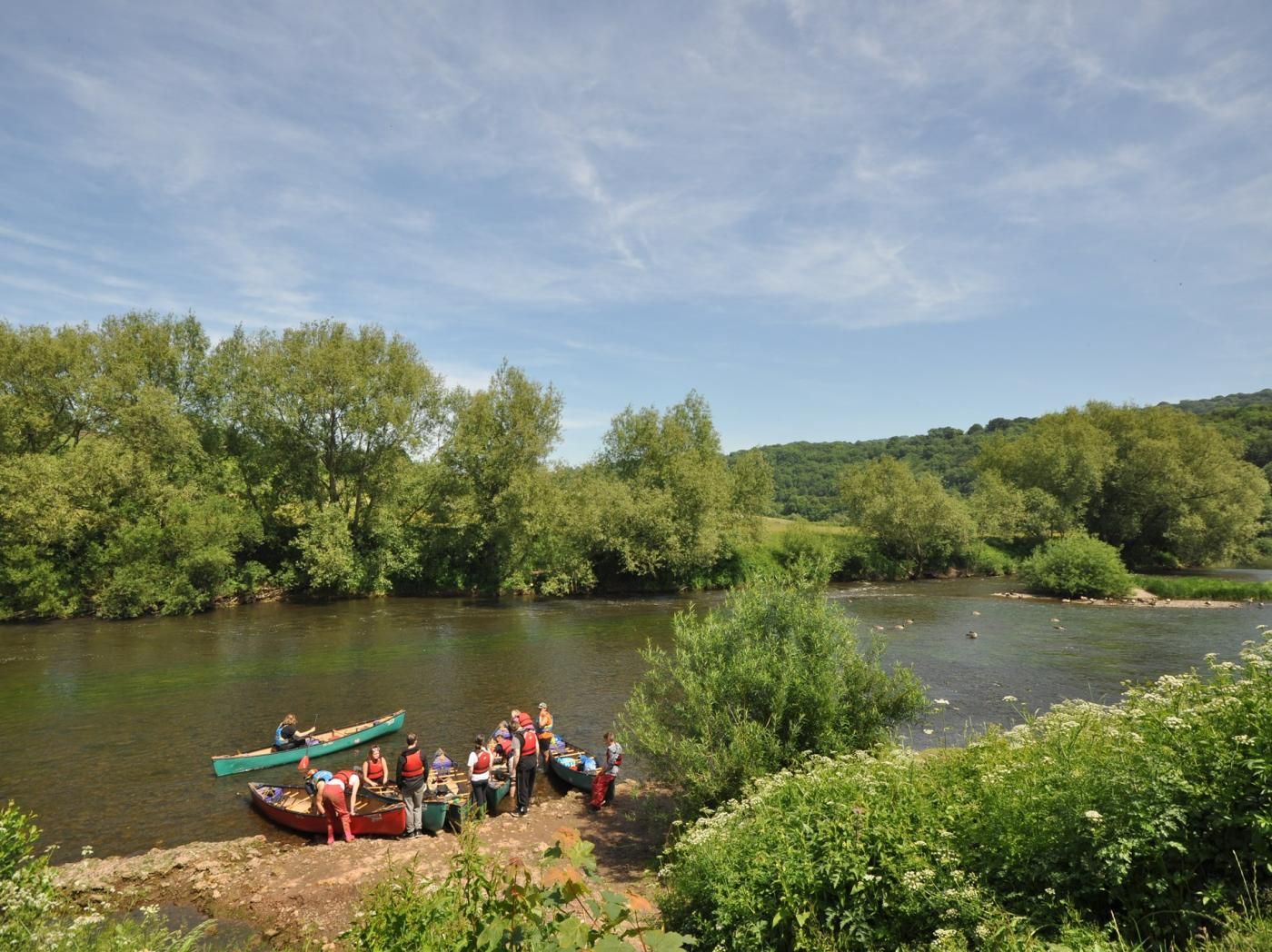 A group of people near a river with canoes, surrounded by greenery and trees.