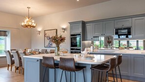 Uma cozinha moderna com armários cinzas, uma ilha central com banquetas, um lustre e uma área de jantar com cadeiras.