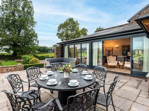 A patio with a round table set for dining, surrounded by chairs. - 4 Bed in Hereford (oc-83768) (Saint Weonards)