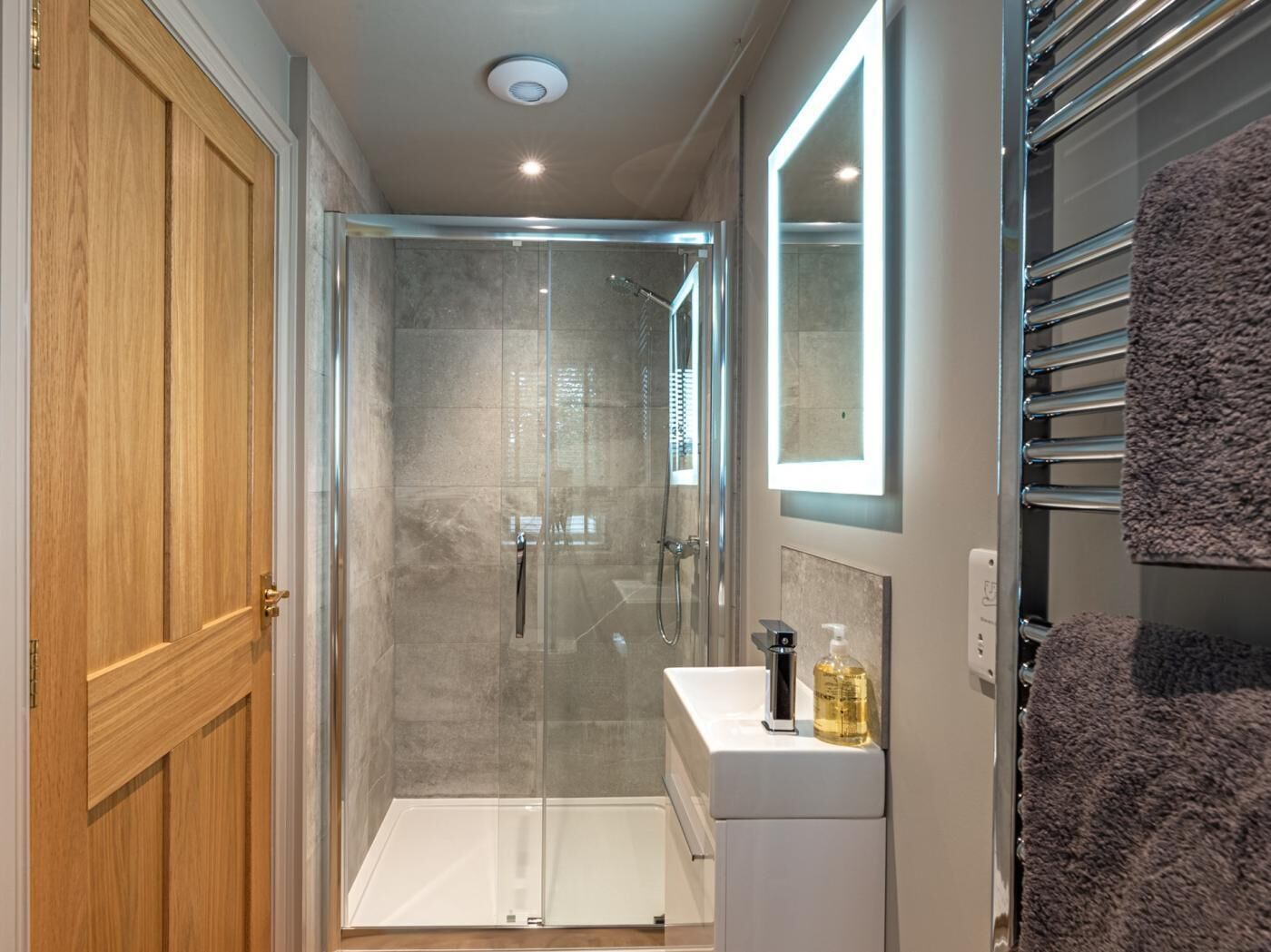 Une salle de bain moderne avec une douche à parois de verre, une porte en bois, un lavabo blanc et un porte-serviettes.