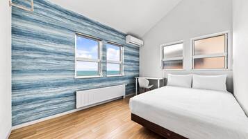 A modern bedroom with a large bed, two windows, a desk, and a view of the sea.