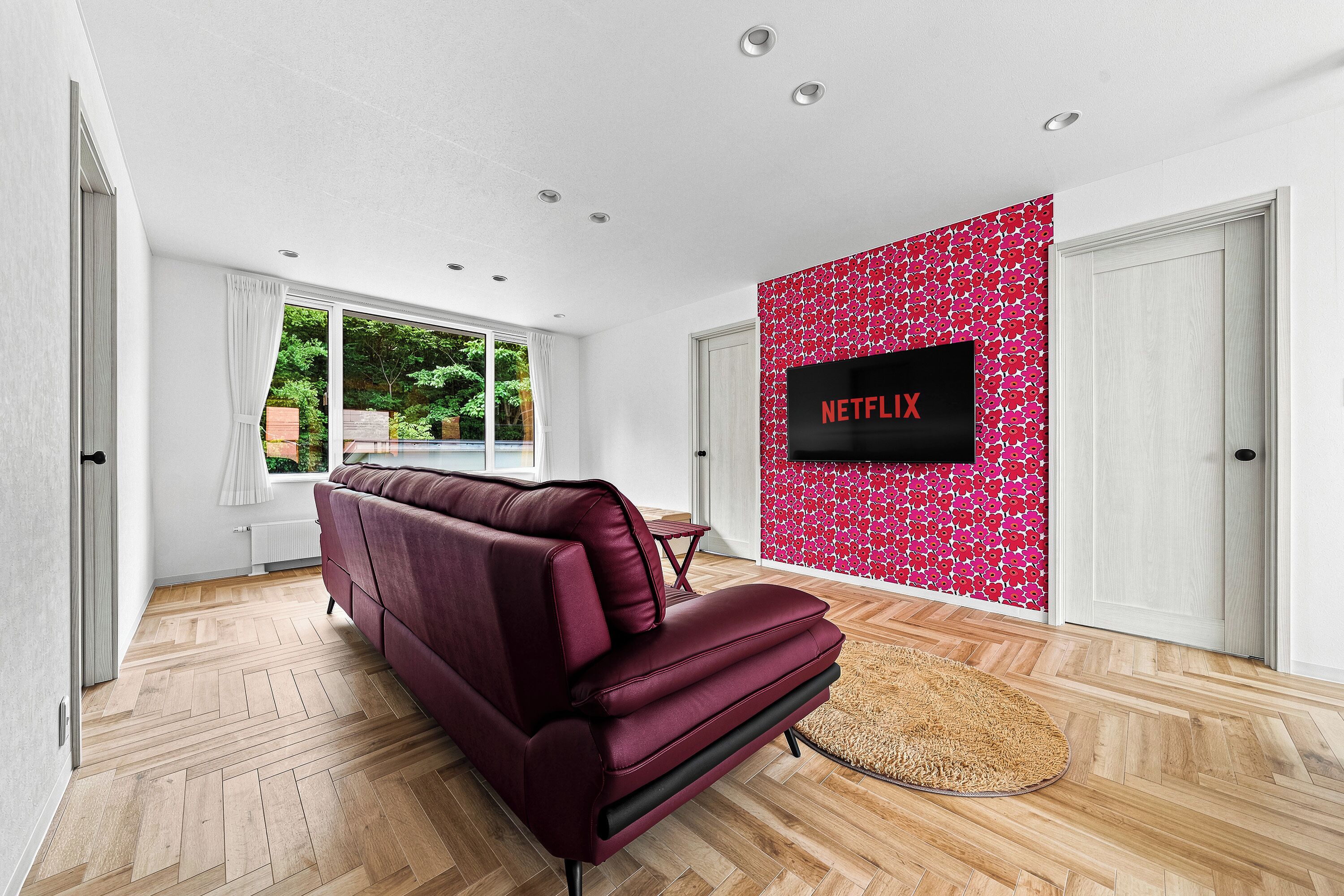Una sala de estar moderna con un sofá rojo, un televisor de pantalla plana montado en una pared con estampado floral rosa y un suelo de madera con motivo de espiga.