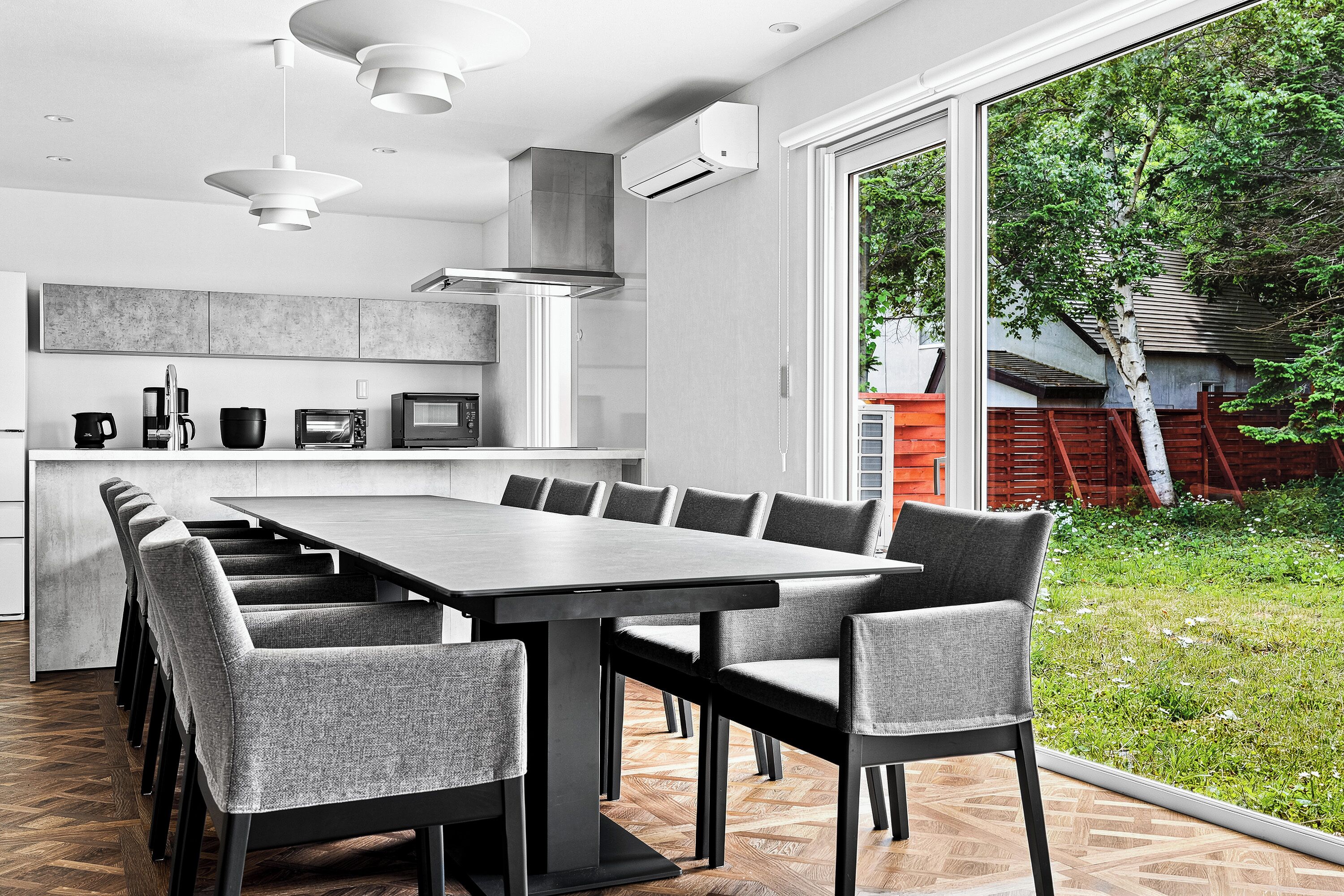 A modern kitchen with a large dining table and chairs, a built-in oven, and a view of the outdoors.