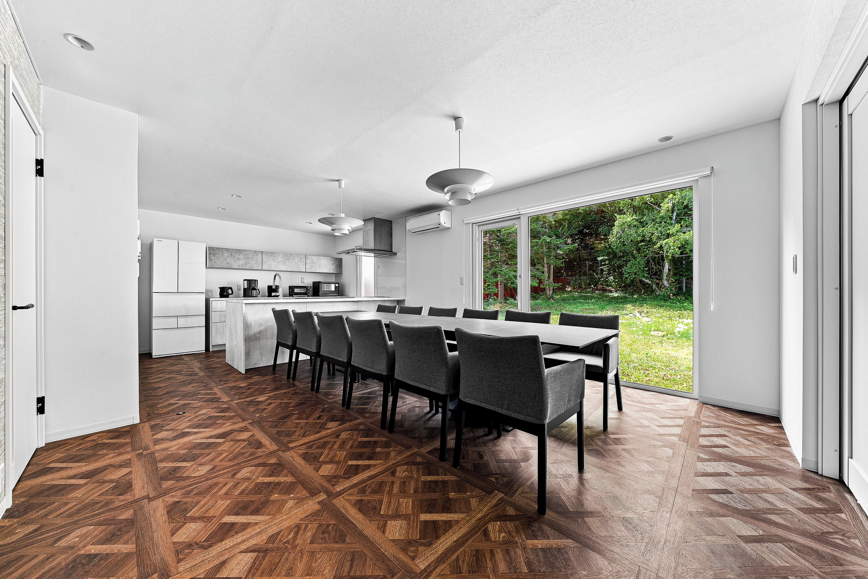 A modern kitchen with white cabinets, a dining area with a long table and chairs, and a large sliding glass door leading to a garden.