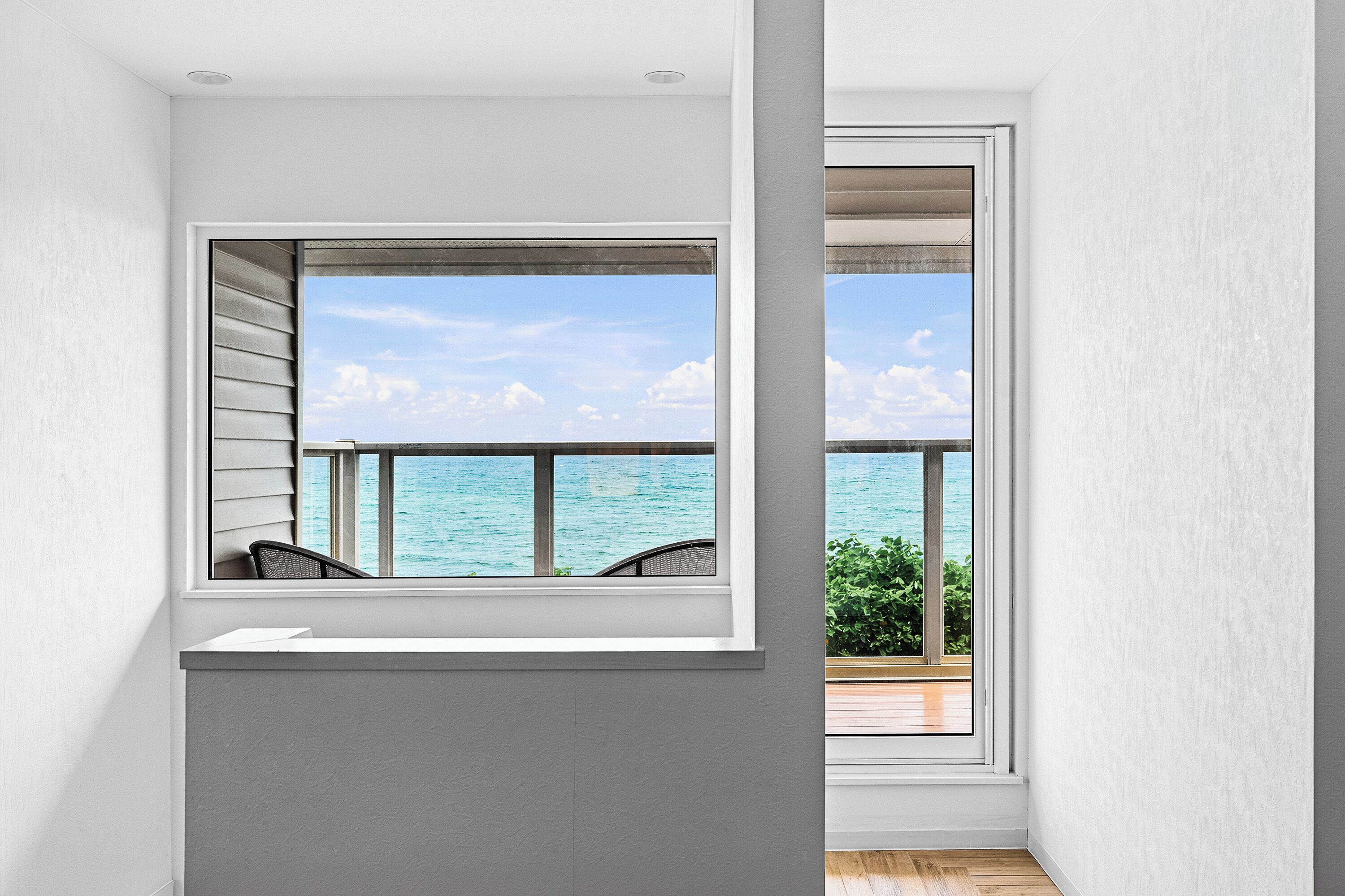 A room with a large window overlooking the sea, a small seating area, and a view of the ocean.