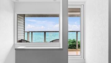 A room with a large window overlooking the sea, a small seating area, and a view of the ocean.