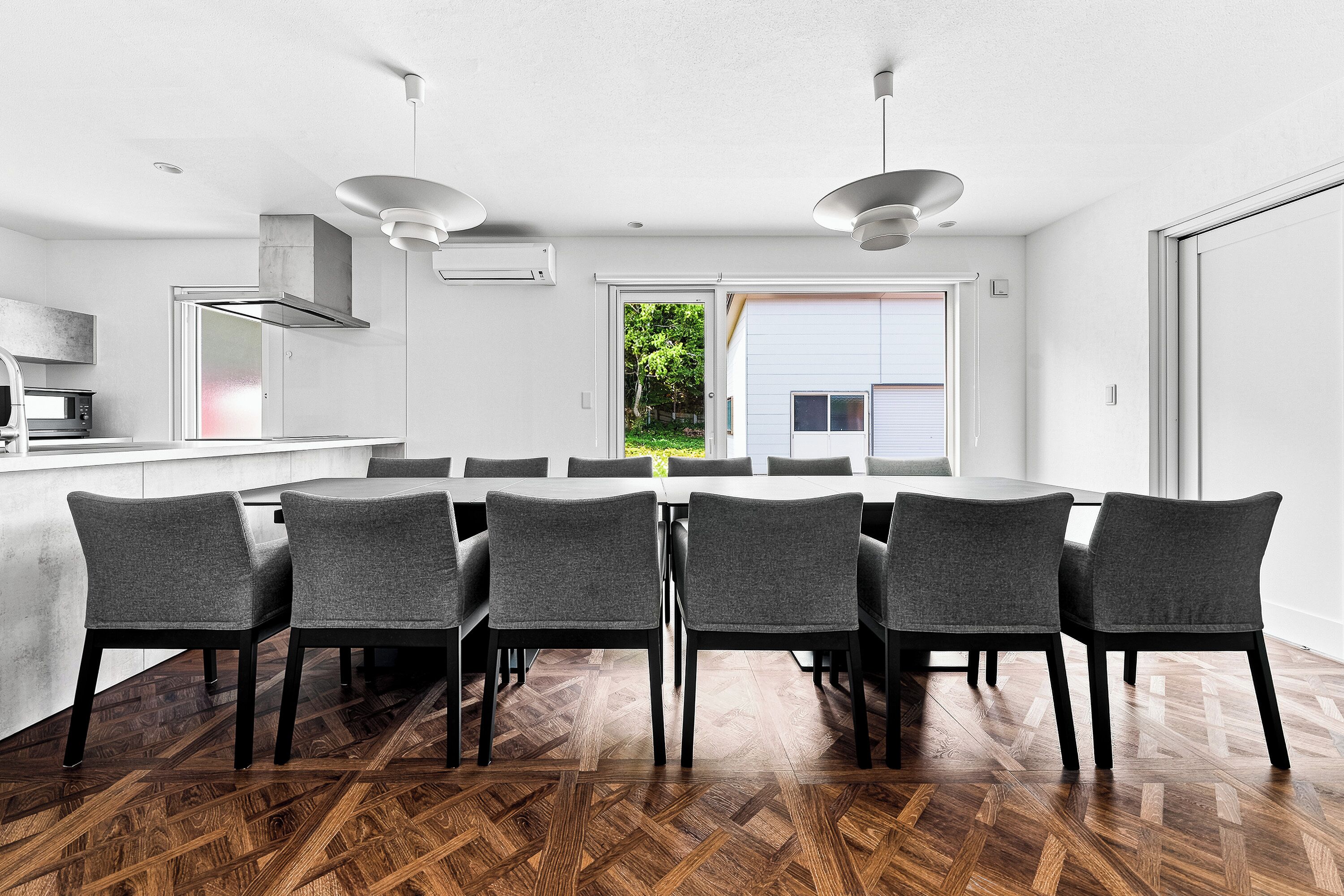 Una cocina moderna con comedor, que presenta un gran mesa y sillas, horno empotrado y vista al exterior.