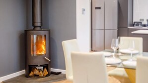 Un intérieur moderne avec un poêle à bois, un coin repas comprenant des chaises et une table, et une cuisine équipée d’un réfrigérateur.