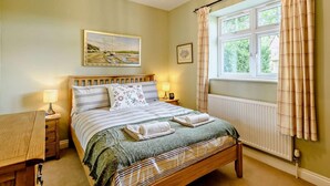 Quarto com cama de madeira, mesa de cabeceira com abajur, janela com cortinas e um quadro na parede.
