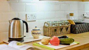 Uma bancada de cozinha com uma chaleira, uma panela, uma cesta de potes e alguns vegetais.