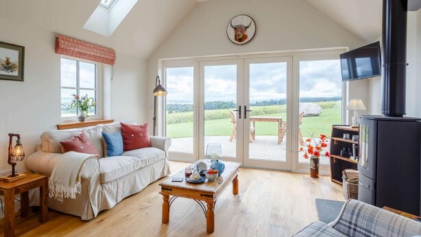 Een ruime woonkamer met een hoge plafond, een open haard, een bank, een bijzettafeltje en een grote schuifpui naar een buitenruimte.