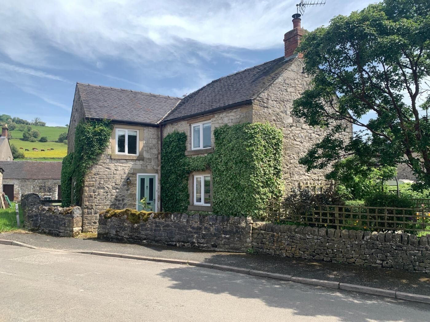 A stone house with a sloped roof, a stone wall, and a small garden.