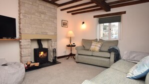 A cozy living room with a stone fireplace, a sofa, a lamp, and a television. - 4 Bed in Matlock (oc-85450) (Brassington)