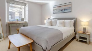 Quarto com cama, escrivaninha, cadeira, mesa de cabeceira e janela com persianas.