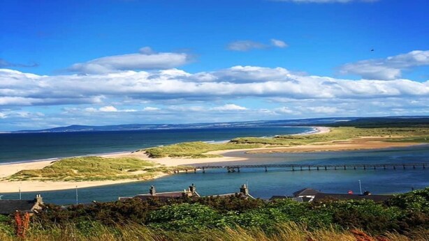 Paisagem costeira com uma praia, um cais e céu claro.