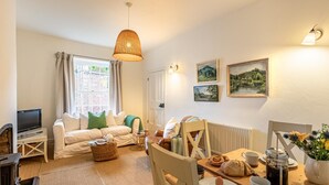 Een gezellige woonkamer met een bank, een eettafel gedekt voor het ontbijt, een televisie en kunstwerken aan de wanden.