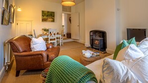 Een gezellige woonkamer met een open haard, een leren fauteuil en een groene gebreide plaid.