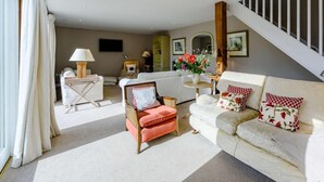 Uma sala de estar ampla, com sofá, poltrona e área de jantar com mesa e cadeiras.
