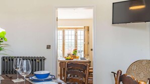 A dining area with a table set for four, a radiator, a television mounted on the wall, and a view through a doorway. - 3 Bed in Whitby (oc-85927) (Fylingdales)