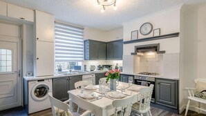 A modern kitchen with a dining area, built-in appliances, and a clock on the wall. - 4 Bed in Holmfirth (oc-86032) (Holmfirth)