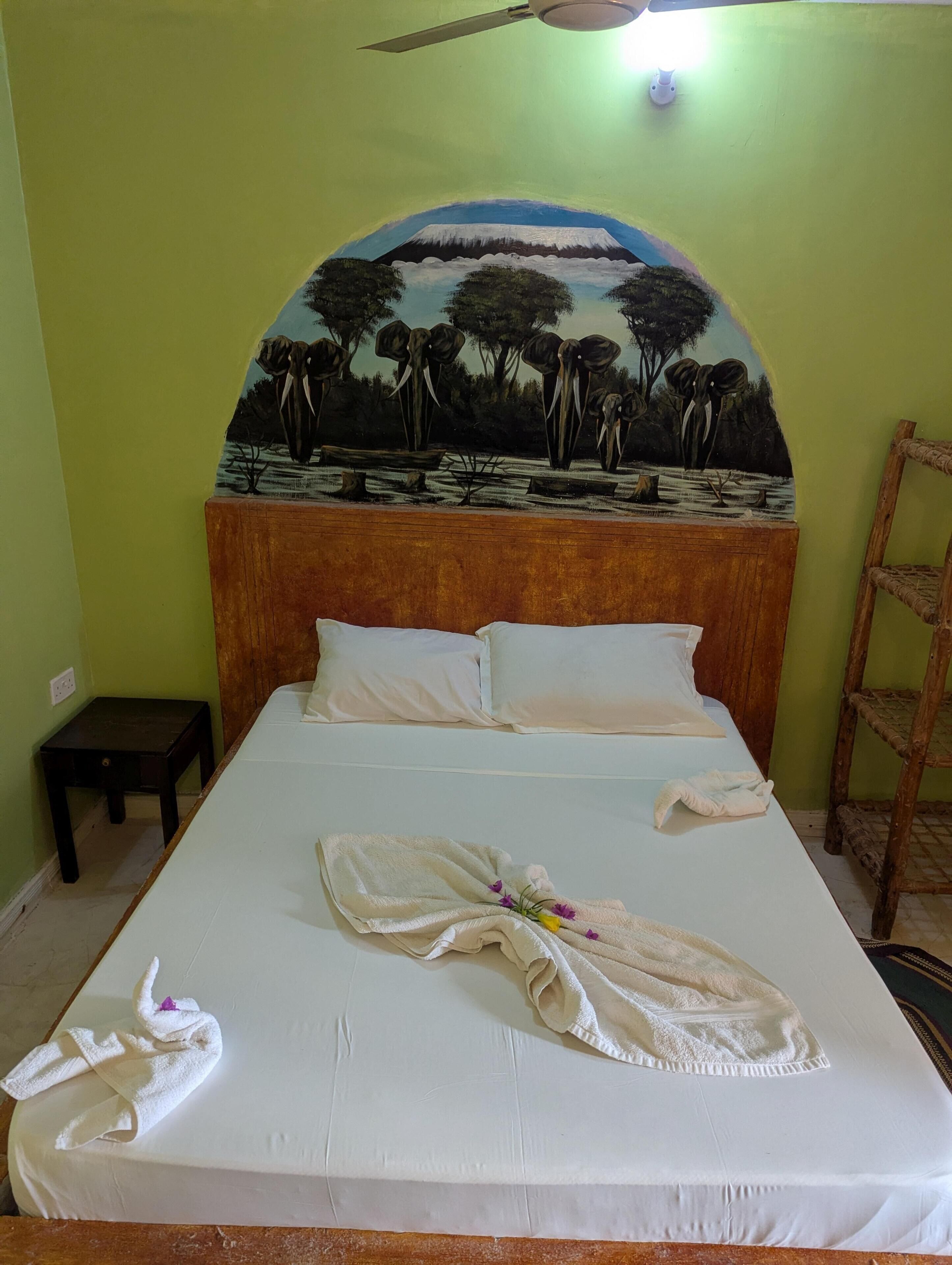 A bed with a headboard featuring a painted landscape, a small wooden nightstand, and a ladder against the wall.