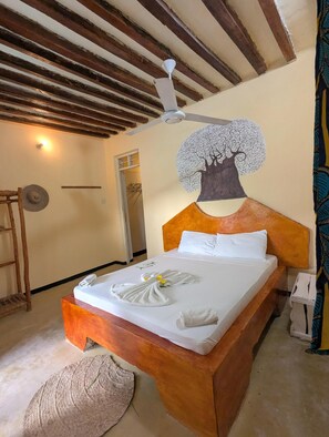A bed with a headboard, a ceiling fan, and a wall with a tree mural. - Villa Molly (Jambiani)
