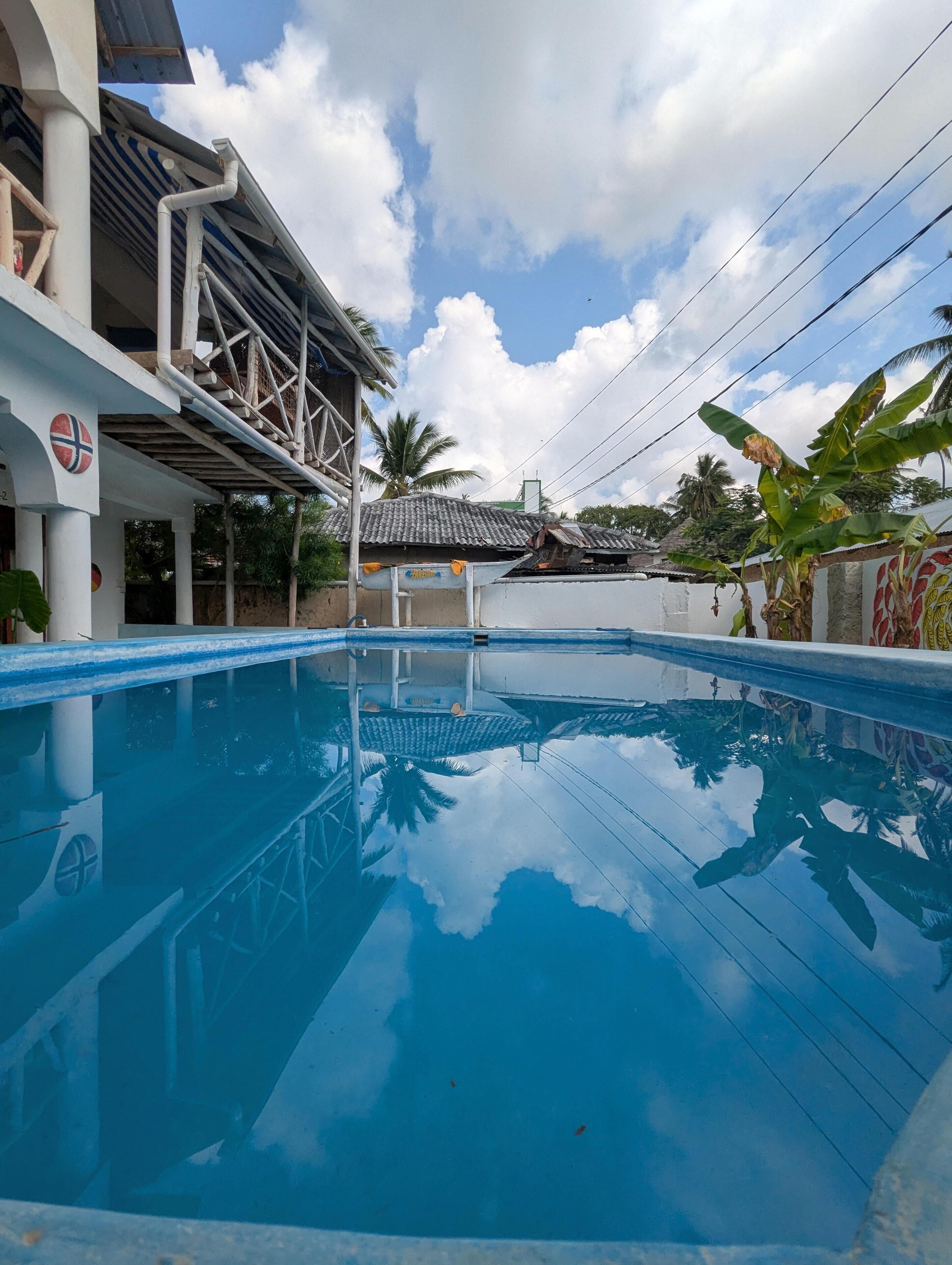 A swimming pool with a clear blue water surface, surrounded by a building with a tiled roof and a flag.