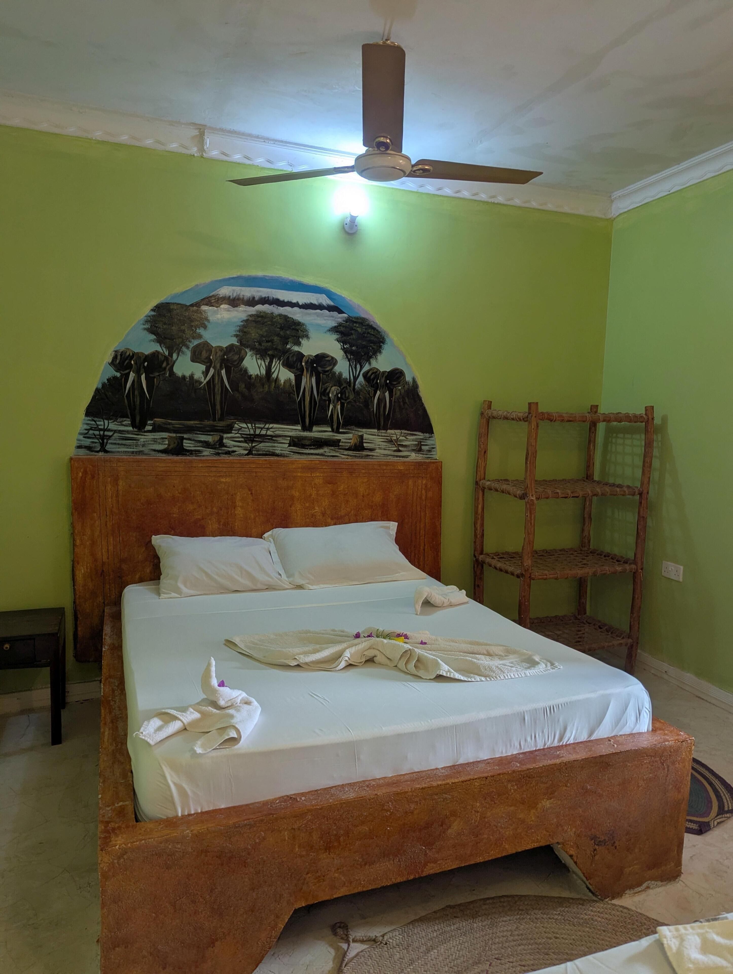 A single bed with a wooden frame and white bedding, a ceiling fan, and a wall-mounted shelf.