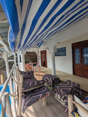 A covered outdoor seating area with wooden furniture and a blue-striped awning.