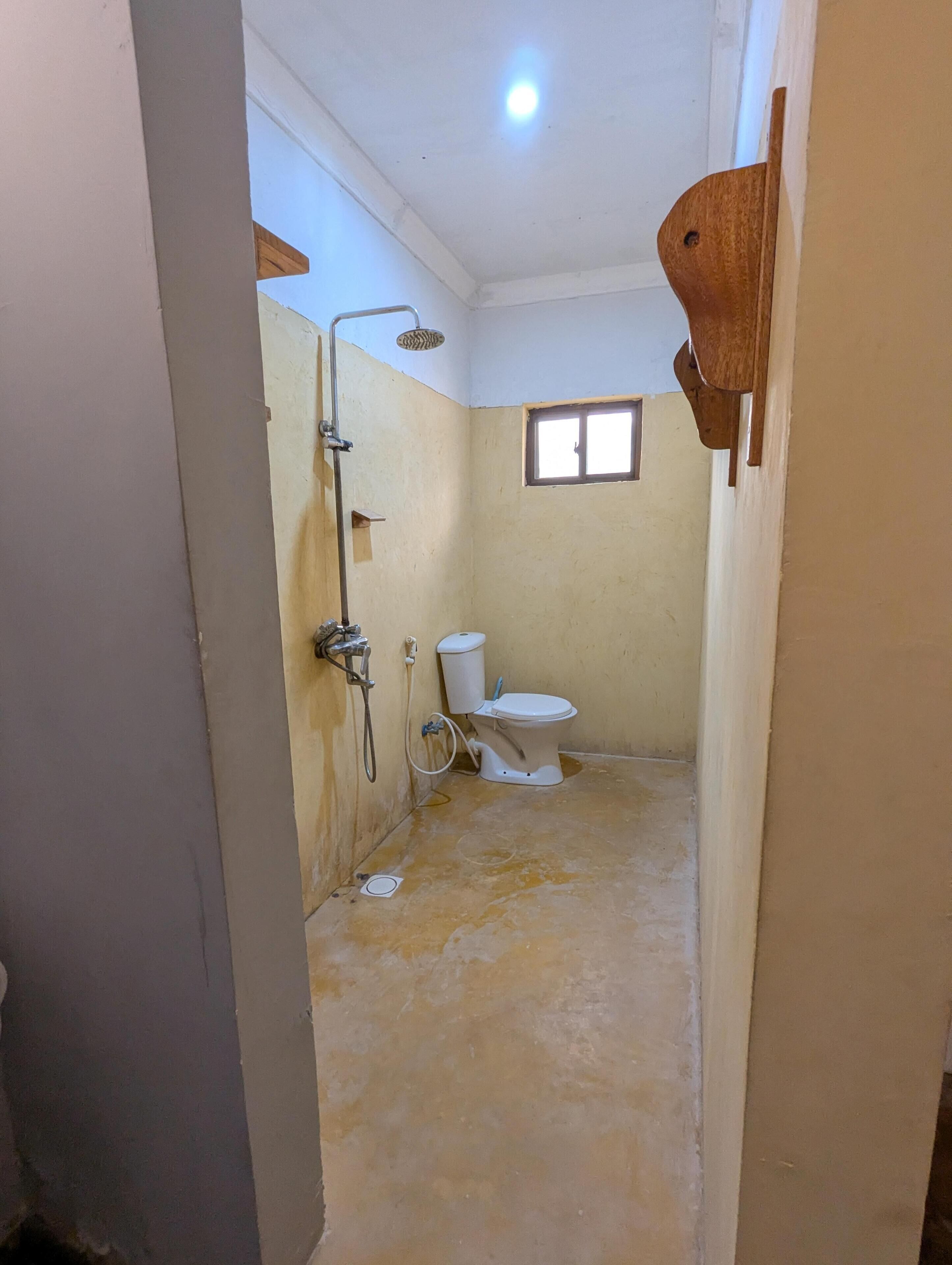 A bathroom with a toilet, shower, and a window.