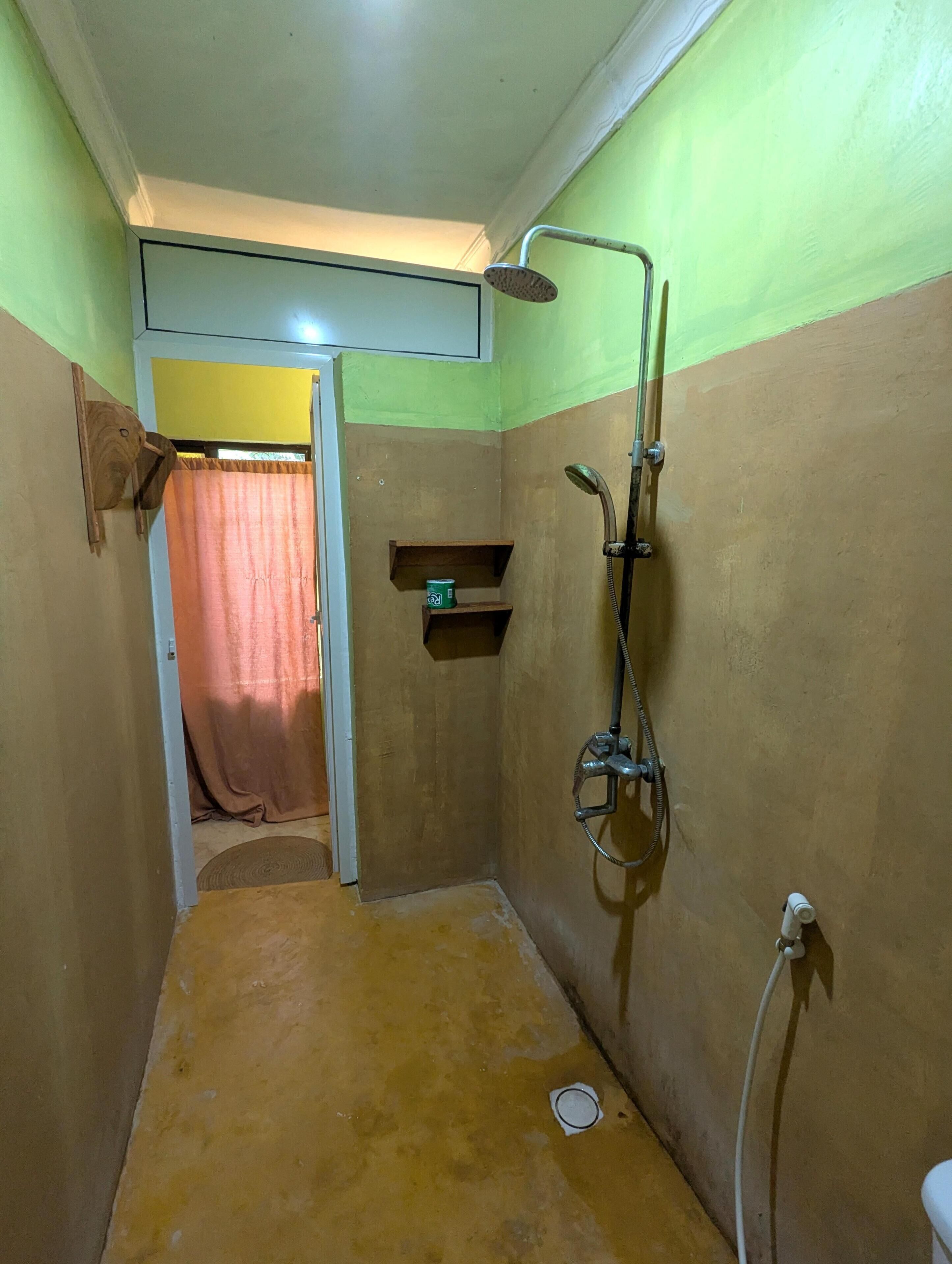 A small bathroom with a shower, a toilet, and a shelf with a can.